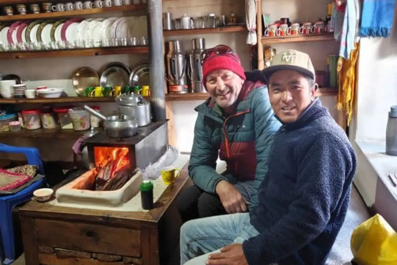 Trekkers and a local guide warming up by a wood stove in a teahouse on the Annapurna Base Camp Trek.